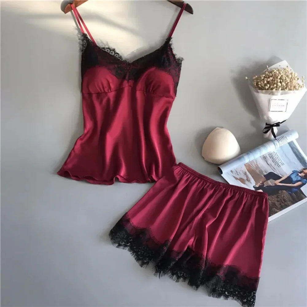 Burgundy satin cami and shorts pajama set with black lace trim, flat lay on gray surface