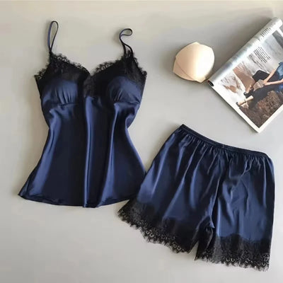 Navy satin cami and shorts pajama set with black lace trim, flat lay on gray surface