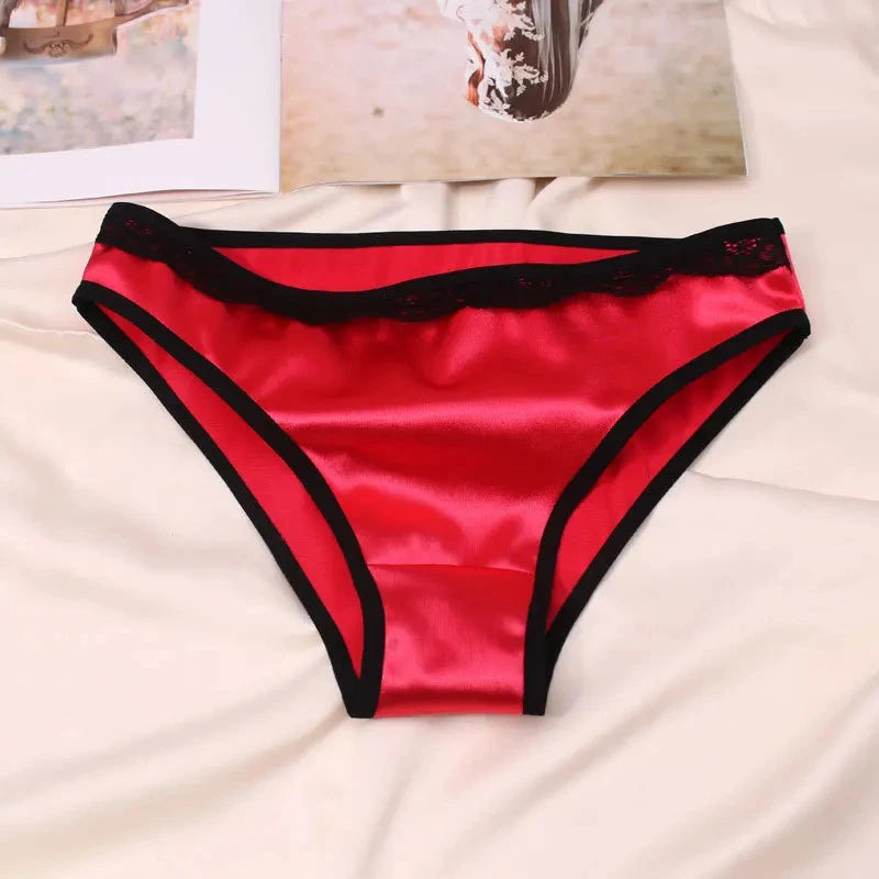 Red satin bikini panties with black lace waistband trim and black binding edges, flat lay on white fabric