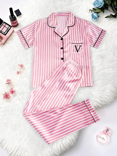 Flat lay front view of pink and white striped satin short-sleeve pajama set with black piping and V-logo chest pocket