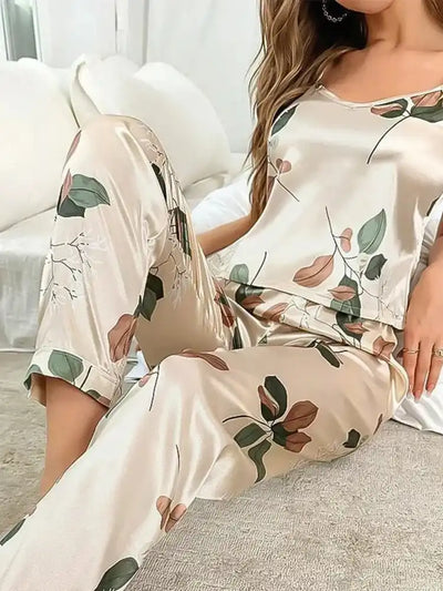 Woman on sofa wearing short-sleeve champagne satin pajama set with botanical leaf print and wide-leg pants