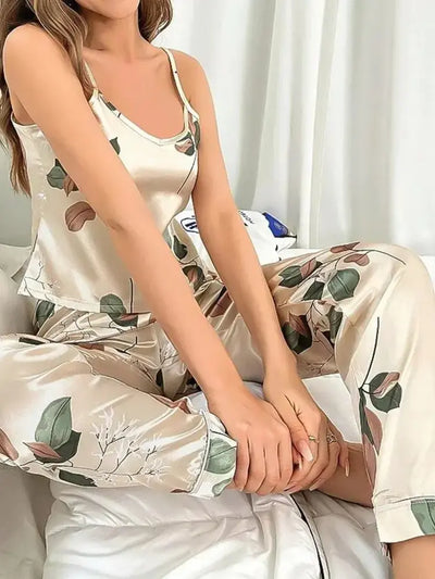 Close-up of woman sitting on bed in champagne satin V-neck cami pajama set with leaf print detail