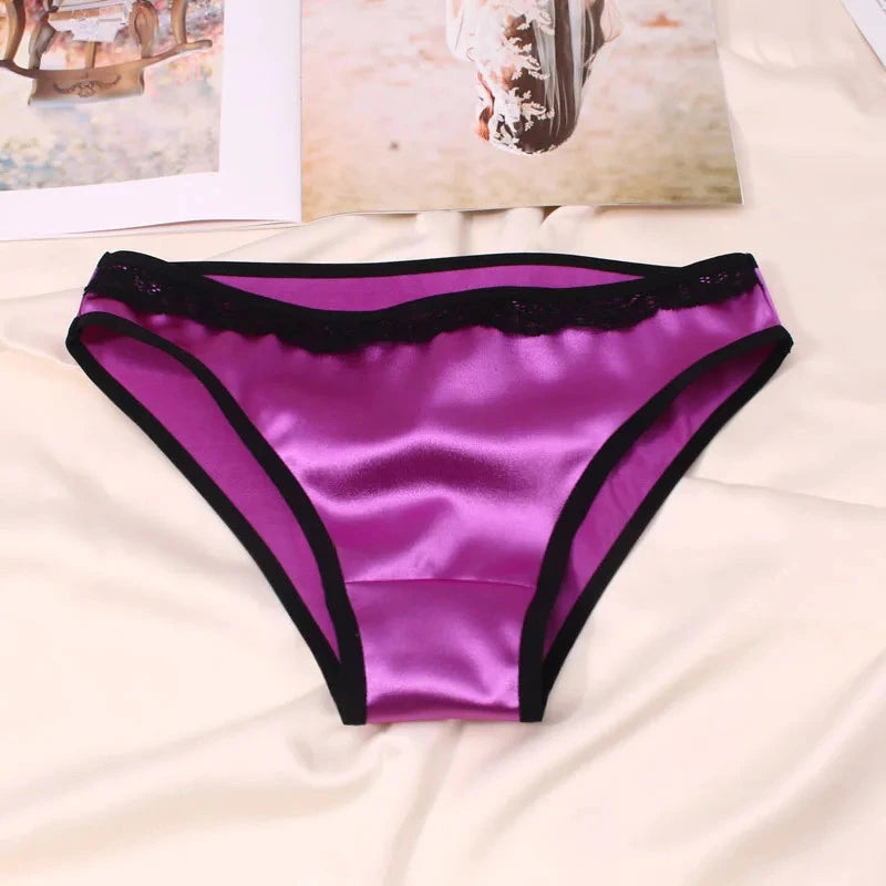 Deep purple satin bikini panties with black lace waistband and contrast trim edging, flat lay on cream fabric