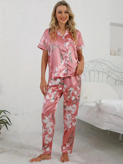 Woman smiling in full-length pink lily-print satin pajama set, front view in bedroom setting