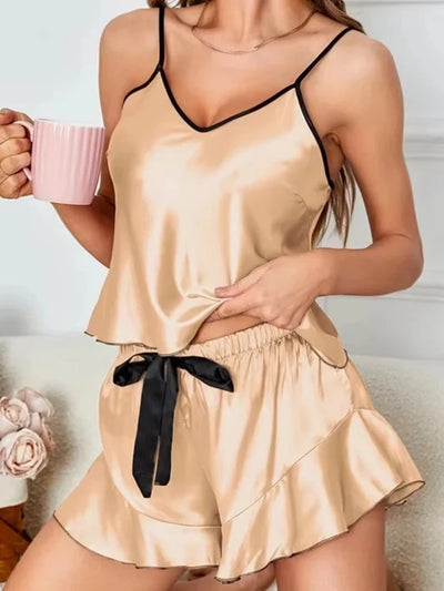 Woman wearing champagne satin cami and ruffle shorts pajama set with black contrast trim, holding a pink mug