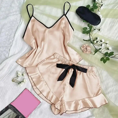 Champagne satin pajama set with ruffle shorts and black ribbon tie, flat lay with roses and sleep mask