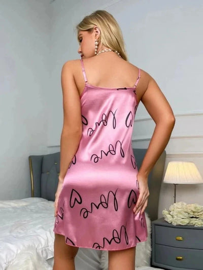 Back view of pink satin nightgown showing adjustable spaghetti straps and all-over black love heart print, mini length