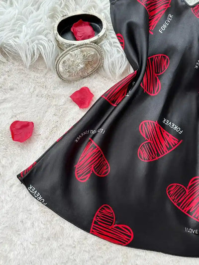 Flat lay of black satin nightgown hem with red heart print and rose petals on white fur