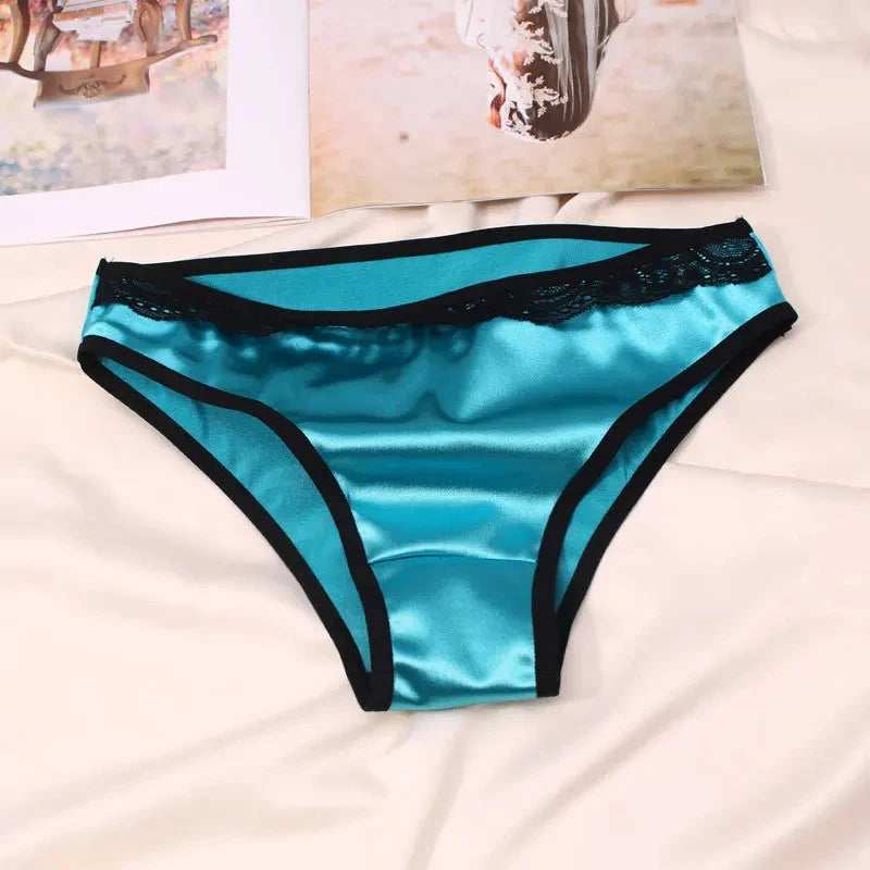 Teal satin bikini panties with black lace waistband trim and black binding on a white bed surface