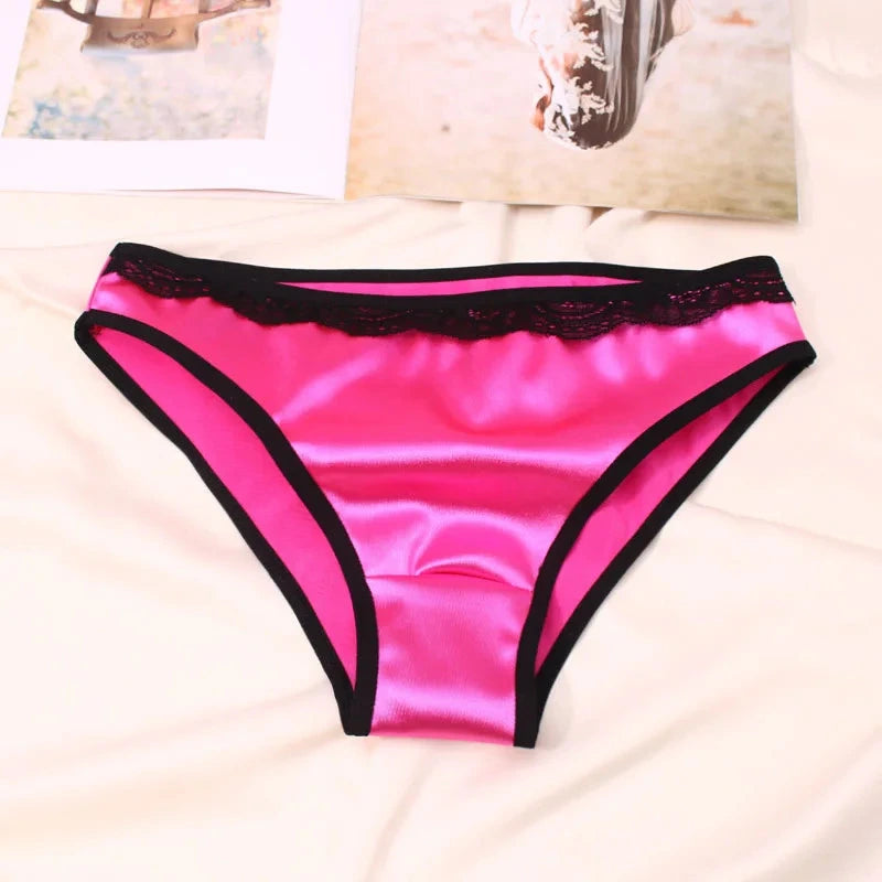 Hot pink satin bikini panties with black lace waistband trim and edge binding, flat lay on white bedding