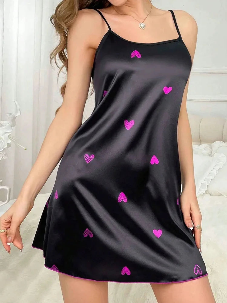 Black satin mini nightgown with adjustable straps and scattered embroidered hot-pink hearts on a woman