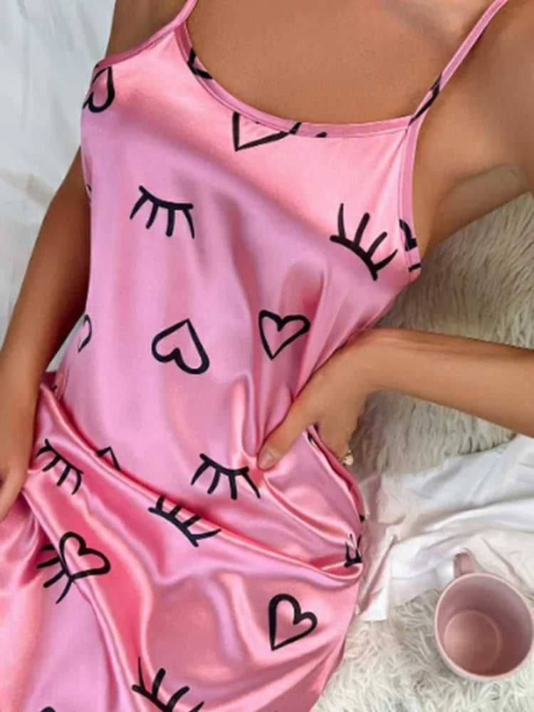 Pink satin nightgown with winking eye and heart print worn by a woman reclining on white bedding with a pink mug nearby