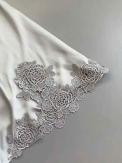Detail of gray satin nightgown hem with floral rose lace appliqué trim on flat surface