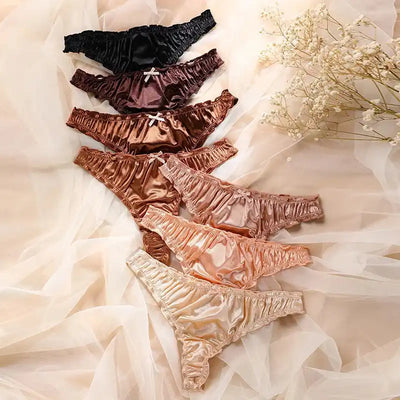 Flat lay of seven satin ruffled thong panties in colors from black to champagne on sheer fabric