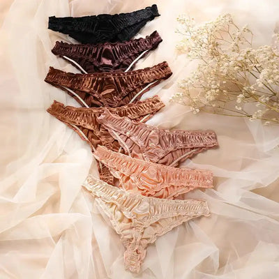 Side angle flat lay of ruffled satin thong panties in gradient shades from black to champagne