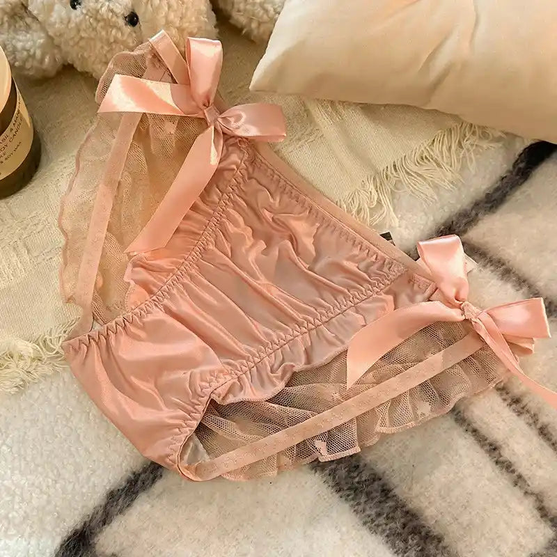 Pink satin bloomer panties with lace trim and four satin ribbon bows on white blanket