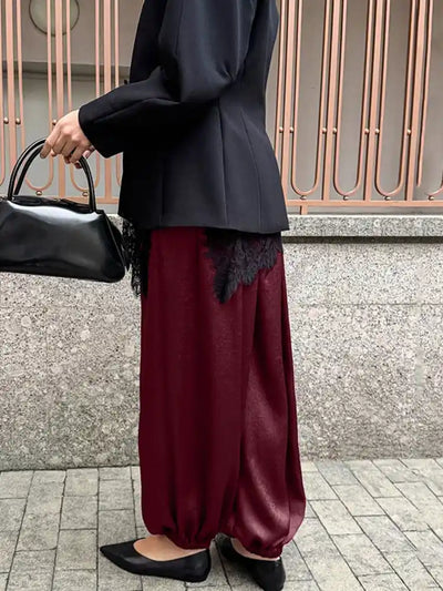 Side view of burgundy fluid wide-leg pants styled with black blazer and structured bag
